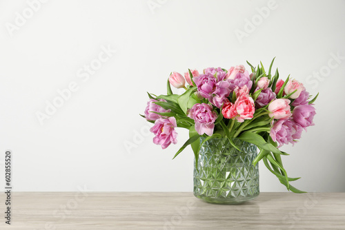 Beautiful bouquet of colorful tulip flowers on wooden table near light wall, space for text