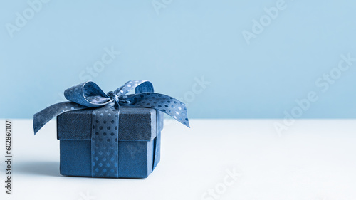 small Luxury gift box with a blue bow on light blue. Polka dot ribbon. Side view monochrome . Fathers day or Valentines day gift. Corporate gift concept or birthday party. Festive sale copy space photo