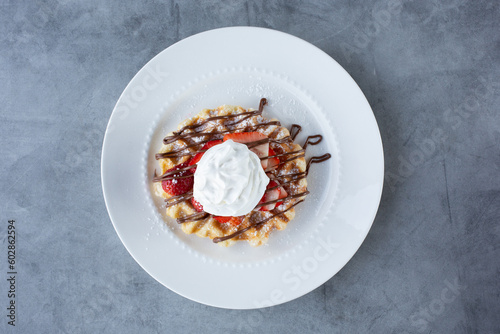 A top down view of a waffle with sliced strawberries  whipped cream and hazelnut spread icing.