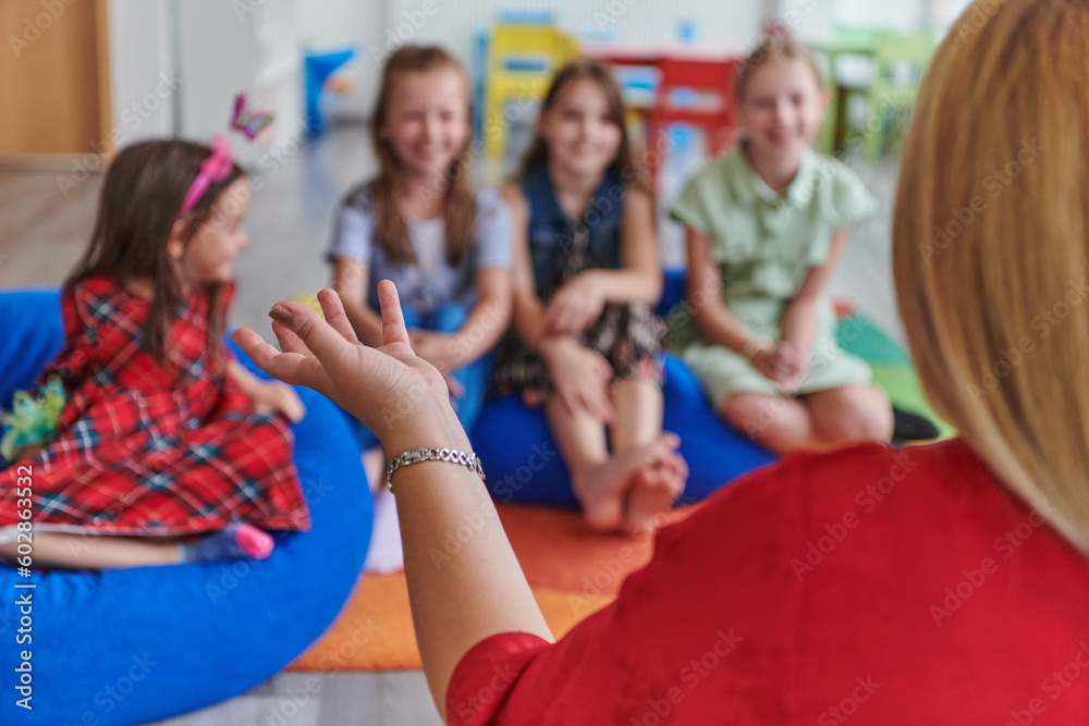 Obraz premium A happy female teacher sitting and playing hand games with a group of little schoolchildren