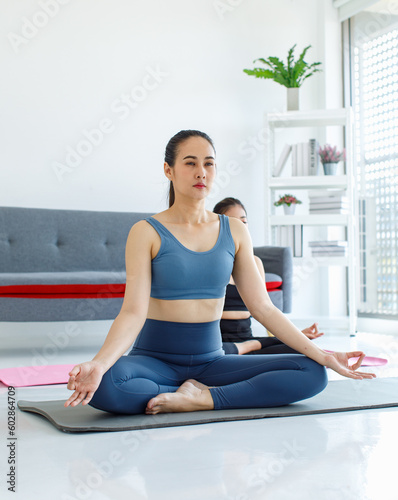 Asian beautiful healthy fit slim female sporty athlete model in sport bra and leggings sitting crossed legs in lotus posture on yoga carpet smiling doing meditation in living room at home with balls