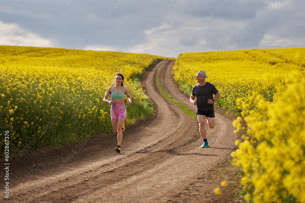 Fototapeta premium Endurance runners on a dirt track in a canola field, training