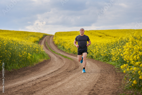 Distance runner running on a road through canola field