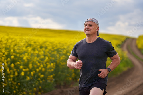 Distance runner running on a road through canola field photo