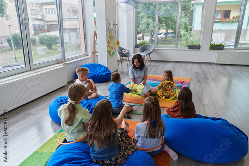 A happy female teacher sitting and playing hand games with a group of little schoolchildren