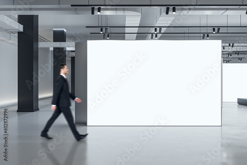 Fototapeta Marketing concept with businessman walking by blank white partition with space f