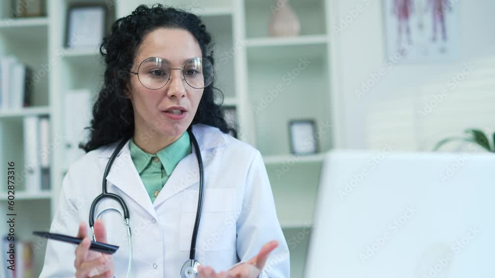 Close up. Confident female doctor in white coat talking on video call using laptop in hospital clinic. Medical worker physician has a conversation with a patient sitting at the workplace in the office Close up. Confident female doctor in white coat talking on video call using laptop in hospital clinic. Medical worker physician has a conversation with a patient sitting at the workplace in the office