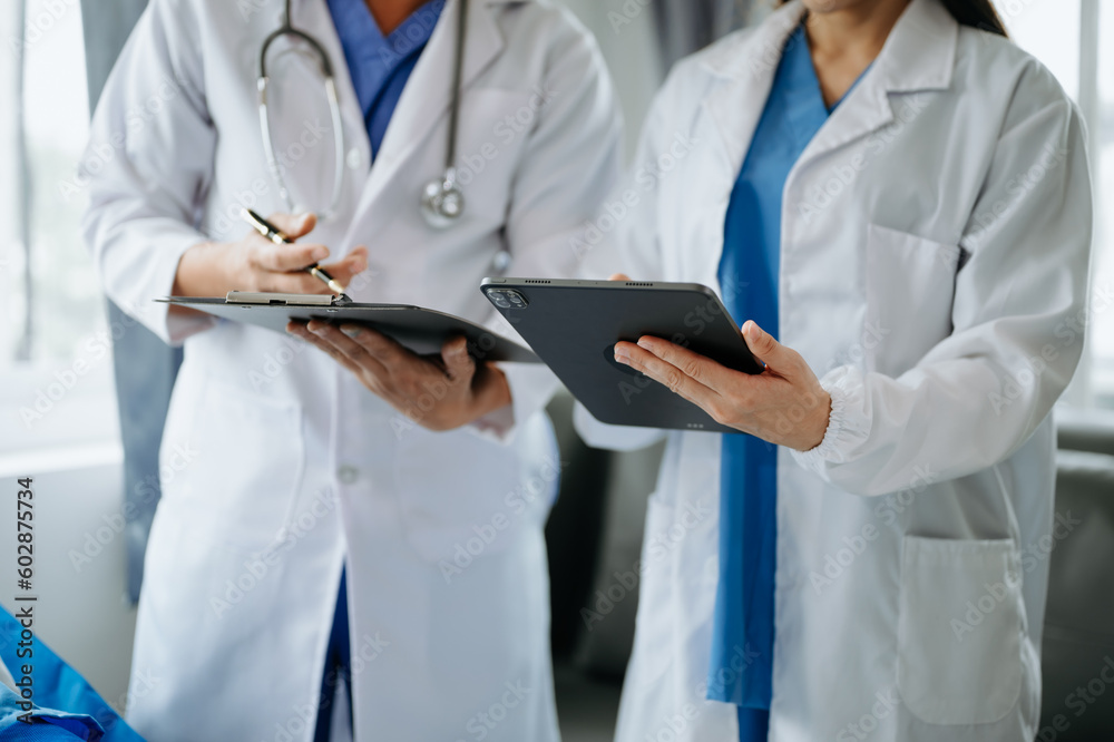 Hospital Ward. Doctor Talks With Professional Head Nurse or Surgeon, They Use Digital tablet Computer. Diverse Team of Health Care Specialists Discussing Test Result Hospital Ward. Doctor Talks With Professional Head Nurse or Surgeon, They Use Digital tablet Computer. Diverse Team of Health Care Specialists Discussing Test Result