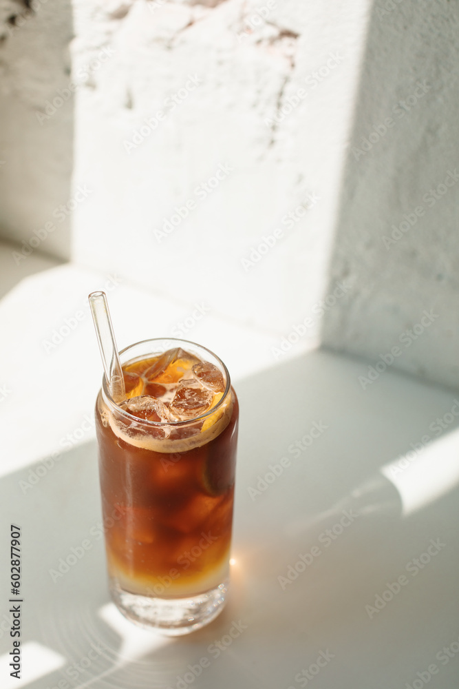 Refreshment summer drink with tonic water, lemon and coffee in tall glass on the table with a sunbeam from the window.