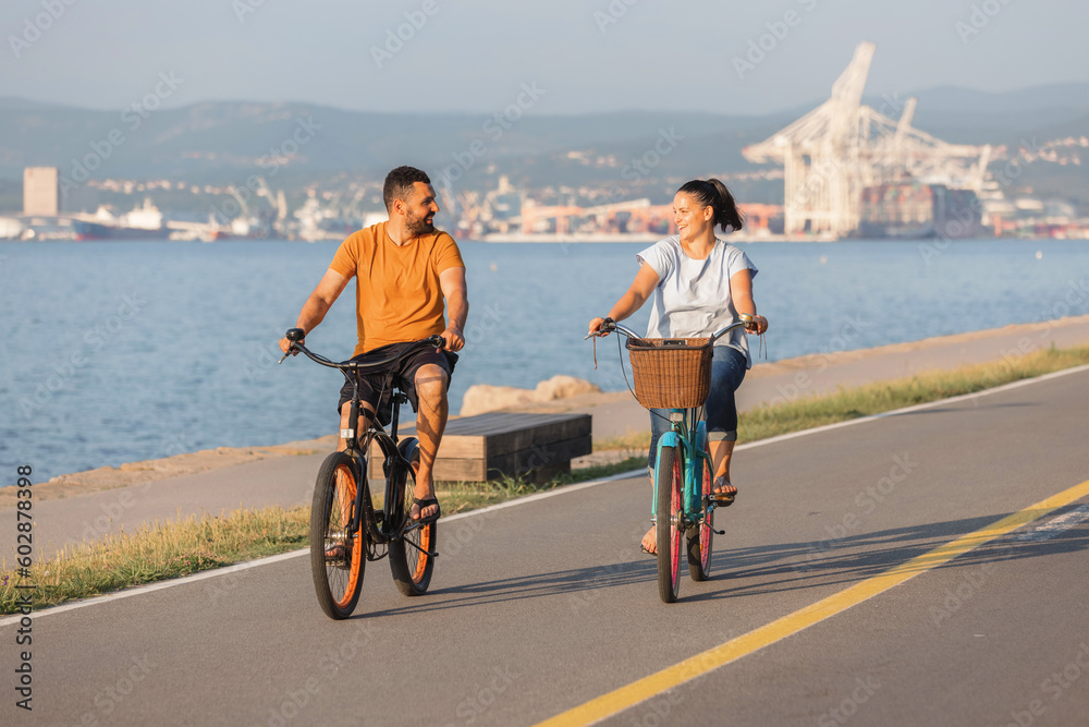 Fototapeta premium Couple taking pleasure in the ride on beach cruiser bikes, pedaling on a wonderful route near the sea