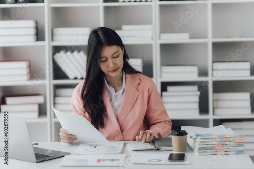 Cheerful business lady working on laptop in office, Asian happy beautiful businesswoman in formal suit work in workplace. Attractive female employee office worker smile.