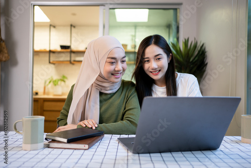 Cheerful girlfriends in had near face smiling while planning further work together and using laptop at home.