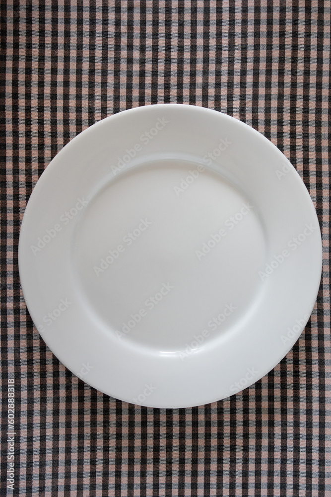 plain empty plate plain size on a traditional brown and black small checkered background, photography for menus and dinner posters. plain empty plate plain size on a traditional brown and black small checkered background, photography for menus and dinner posters.