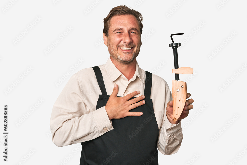 A middle-aged shoe maker laughs out loudly keeping hand on chest. A middle-aged shoe maker laughs out loudly keeping hand on chest.