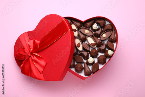 Heart shaped box with delicious chocolate candies on pink background, top view