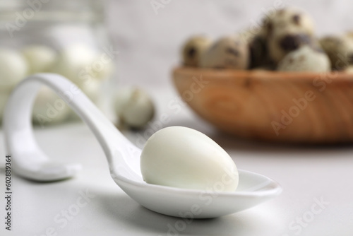 One boiled quail egg in spoon on white table, closeup. Space for text