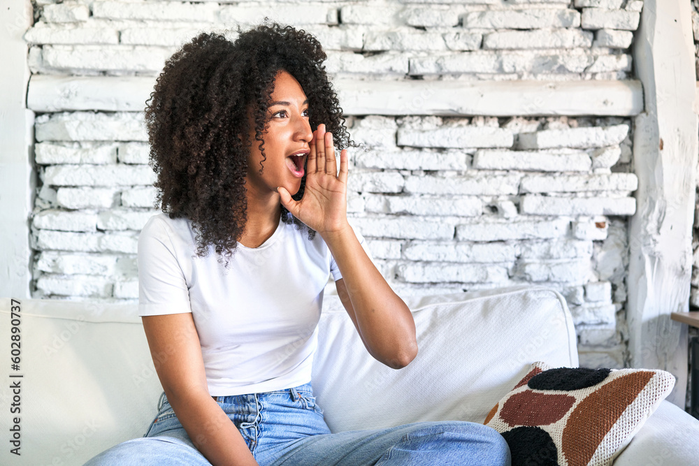 A young african american woman sitting on her sofa shouting and holding palm near opened mouth. A young african american woman sitting on her sofa shouting and holding palm near opened mouth.