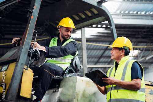 Industrial worker driving a forklift in the factory. Engineer is working and maintaining in the warehouse.