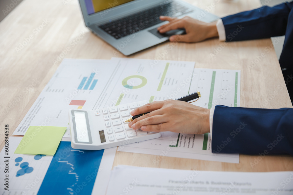 Close-up of asian businesswoman using calculator and laptop for mathematical finance on wooden table, tax, accounting, statistics and analytical research concept Close-up of asian businesswoman using calculator and laptop for mathematical finance on wooden table, tax, accounting, statistics and analytical research concept
