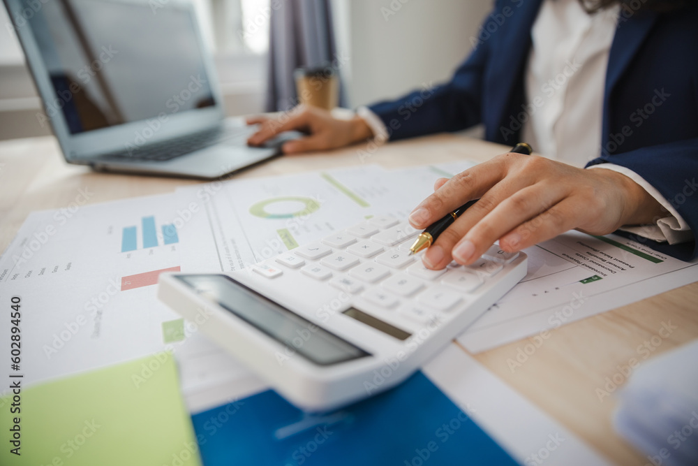 Close-up of asian businesswoman using calculator and laptop for mathematical finance on wooden table, tax, accounting, statistics and analytical research concept Close-up of asian businesswoman using calculator and laptop for mathematical finance on wooden table, tax, accounting, statistics and analytical research concept