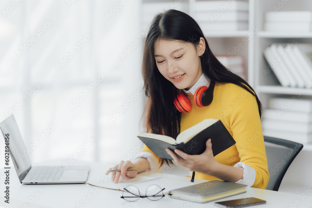 Happy young Asian woman working while reading book in the study room Happy young Asian woman working while reading book in the study room