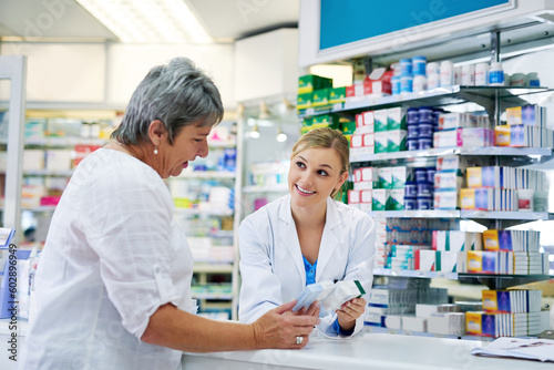 Pharmacist explaining medicine to a woman in the pharmacy for pharmaceutical healthcare prescription. Medical, counter and female chemist talking to a patient about medication in a clinic dispensary photo