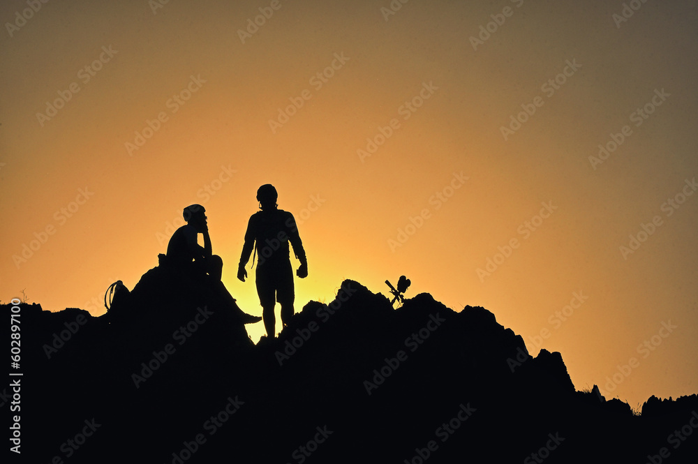 Silhouettes Of A Cyclists Standing on Clif Against The Sun