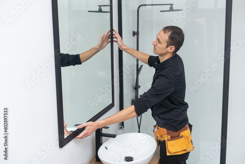 The worker installs the mirror in the bathroom. photo