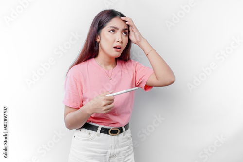 Unhappy woman wearing pink t-shirt looking at pregnancy test alone, confused young female shocked by result, bad news, covering open mouth with hand, unwanted pregnancy concept photo
