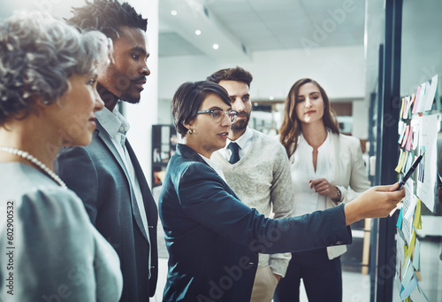 Business people, teamwork or woman writing on board for brainstorming or speaking of solution, ideas or goals. Group planning, sticky note or group with leadership for project collaboration together