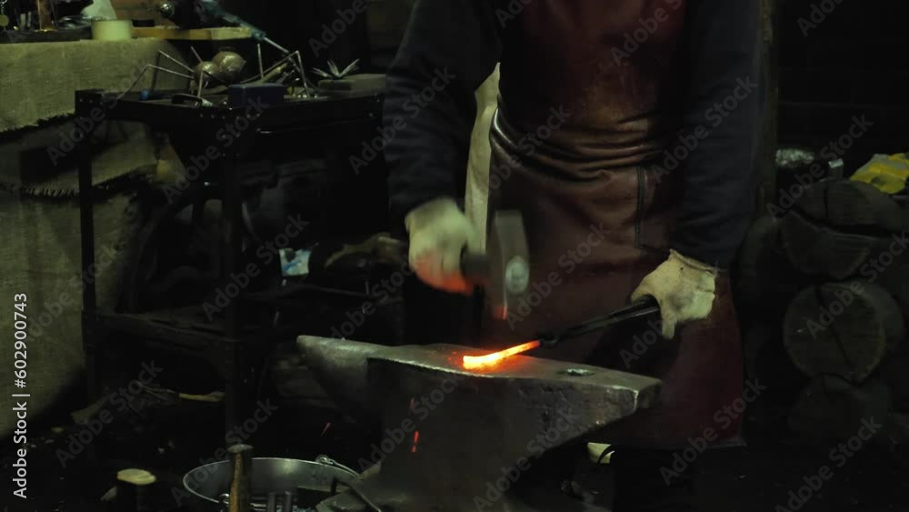 A blacksmith working with molten metal with a hammer on an anvil in a forge. Hard manual work. A blacksmith's workshop A blacksmith working with molten metal with a hammer on an anvil in a forge. Hard manual work. A blacksmith's workshop