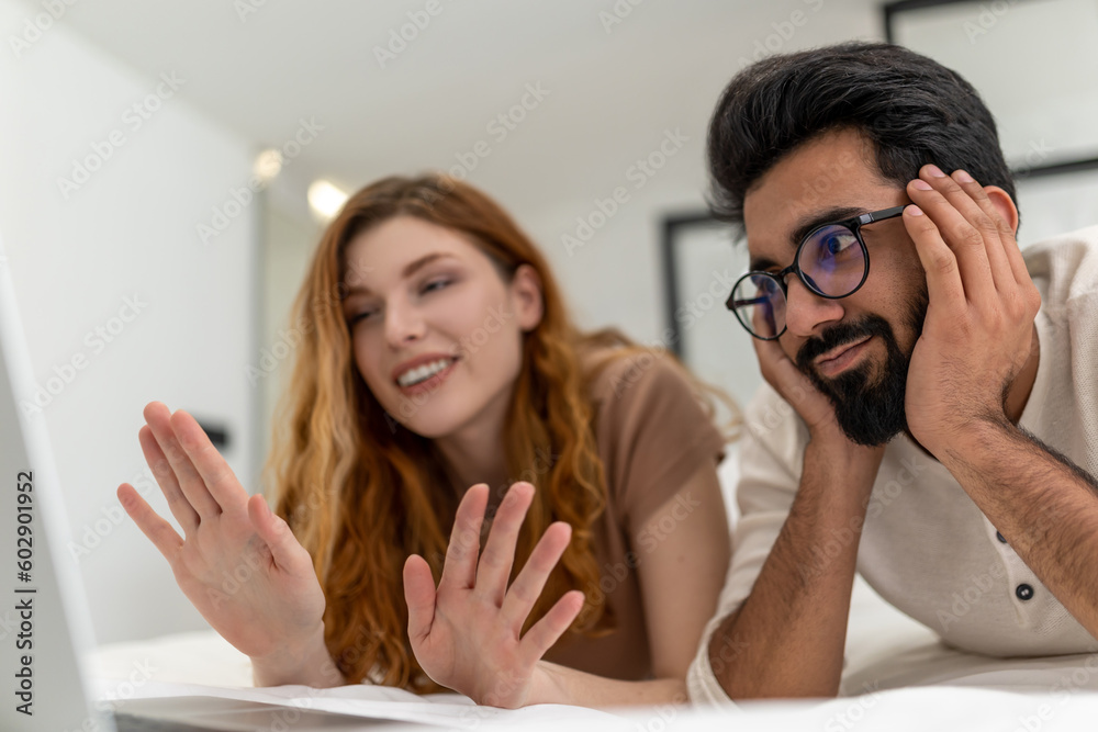Couple enjoy leisure time at home using laptop computer laying on bed having video call waving hand. Couple enjoy leisure time at home using laptop computer laying on bed having video call waving hand.
