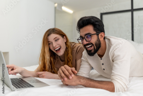 Man and woman spending time at home watching movie on laptop while laying on bed. © zinkevych