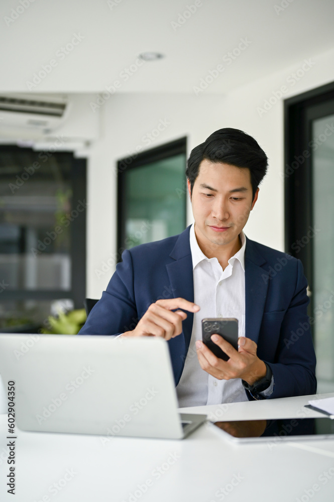 Smart Asian businessman using his smartphone to contact his supplier at his desk. Smart Asian businessman using his smartphone to contact his supplier at his desk.
