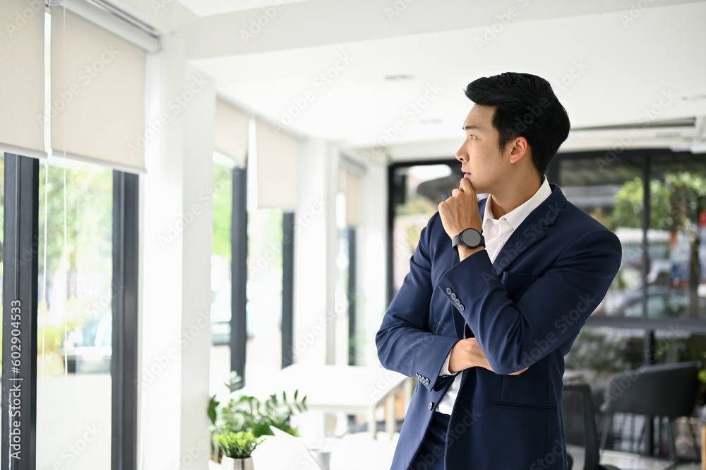 Thoughtful millennial Asian businessman hand on chin, looking out the window Thoughtful millennial Asian businessman hand on chin, looking out the window