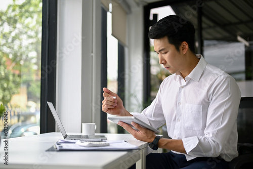 Concentrated Asian businessman managing his work on digital tablet