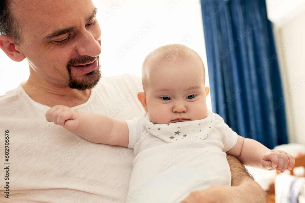 Close-up portrait of happy young father hugging and kissing his sweet adorable newborn child. Indoors shot, concept image. Copy space.