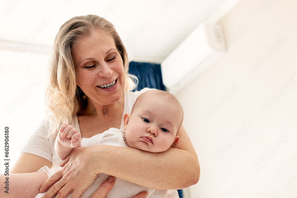 Happy smiling mother holds and hugs her baby in a bright room. Harmonious family, happy motherhood and childhood.