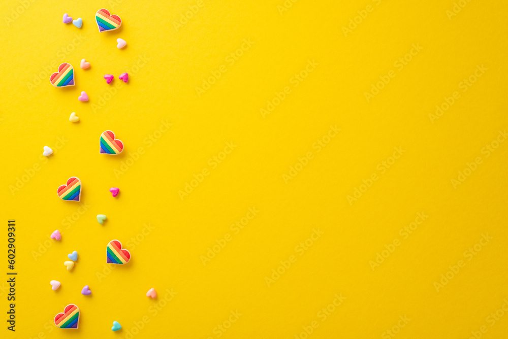 Display your support for the LGBT community with this top view flat lay of parade symbolic accessories on yellow backdrop, featuring rainbow color pin badges, hearts, with a blank space for text or ad