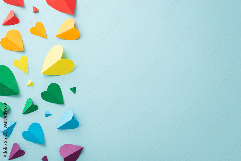 LGBT History Month concept. Top-down shot of symbolic parade accessories, including a rainbow colored paper hearts, laid out on a pastel blue backdrop with space for text - obrazy, fototapety, plakaty 