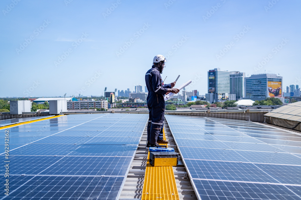 Engineers walking on roof inspect and check solar cell panel by hold blue print  and tablet ,solar cell is smart grid ecology energy sunlight alternative power factory concept.