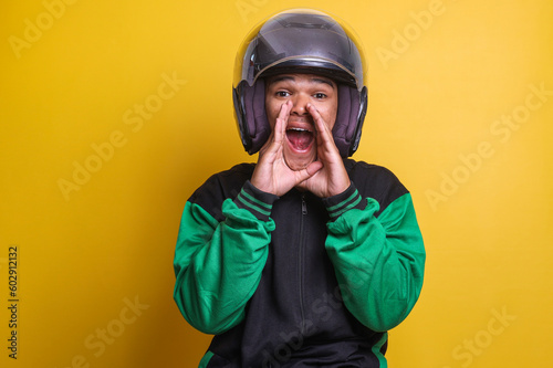 Asian online taxi driver motorbike man with shout gesture or making announcement isolated over yellow background