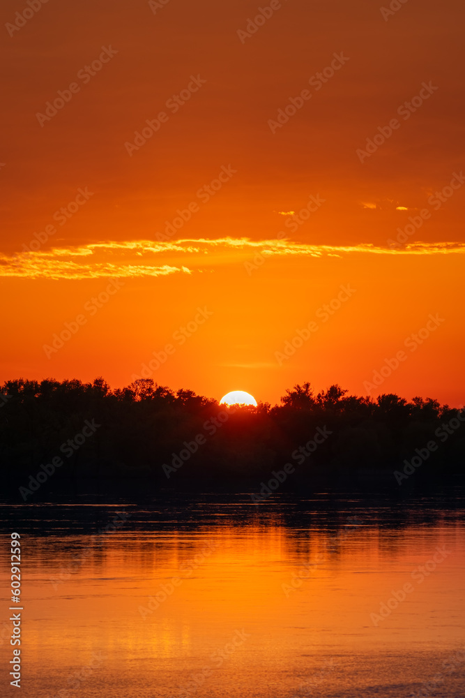 Golden sunset and sunset with clouds over forest and river or lake
