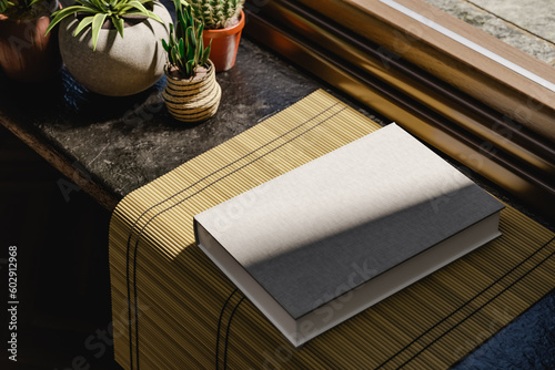 Hard cover book mock up near a window. Daylight interior with plants. 3D rendering