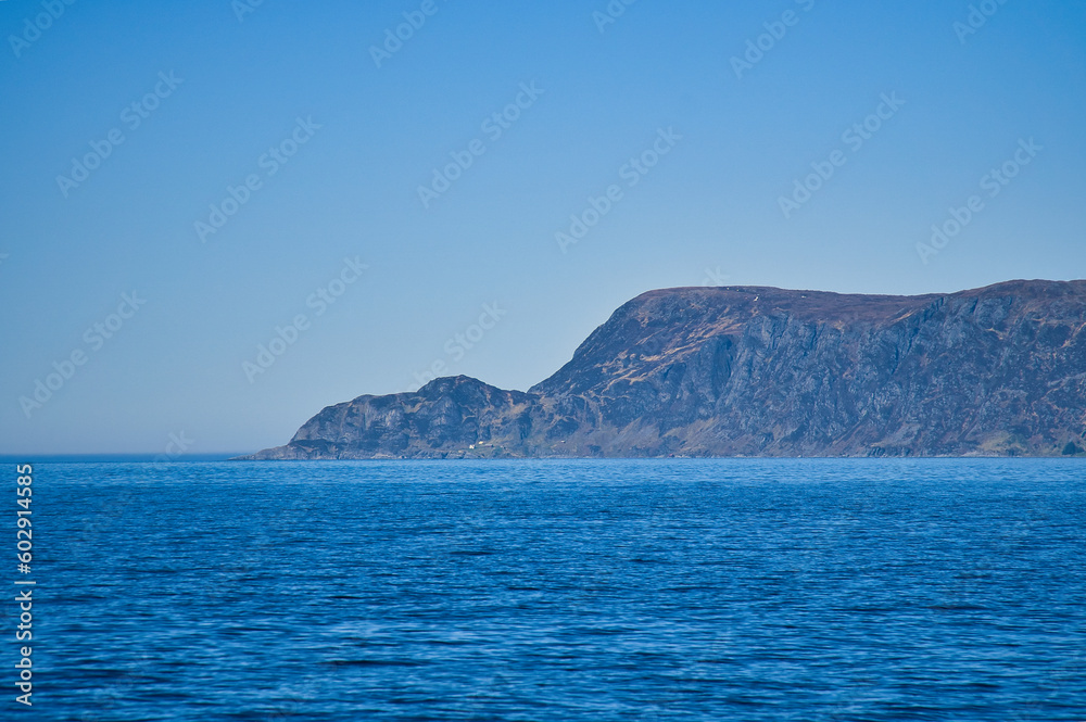 View from the sea to the West Cape in Norway in sunshine. Waves and rocks