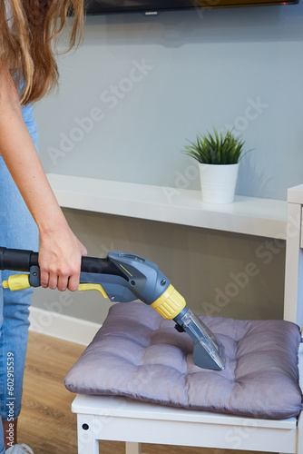 Closeup of a female cleaner cleaning cushions on a chair using a vacuum cleaner