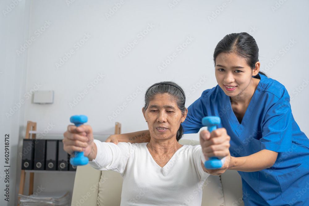 Young pretty asian physiotherapist helping senior female patient holding dumbbell in physical therapy session, concept of World Confederation for Physical Therapy. Young pretty asian physiotherapist helping senior female patient holding dumbbell in physical therapy session, concept of World Confederation for Physical Therapy.