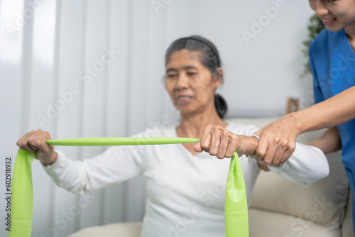Concept of World Confederation for Physical Therapy. young physiotherapist caregiver helping mature elderly woman training with elastics in rehabilitation center, muscle weakness