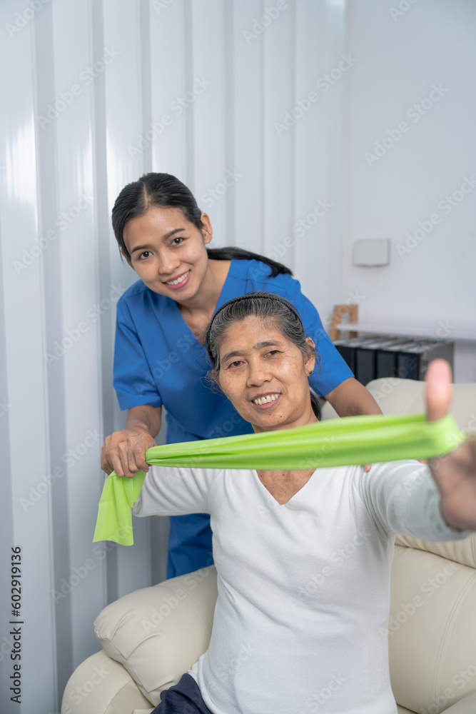 Fototapeta premium Concept of World Confederation for Physical Therapy. young physiotherapist caregiver helping mature elderly woman training with elastics in rehabilitation center, muscle weakness