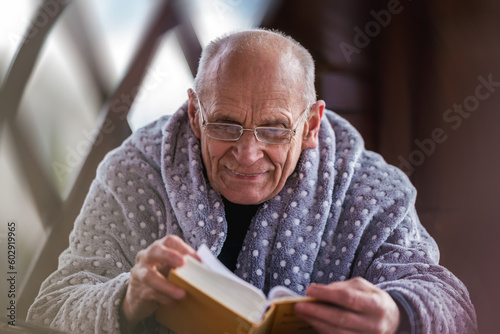 Mature man wearing eyeglasses and cozy plaid reading book outside. Senior people lifestyle and pastime.
